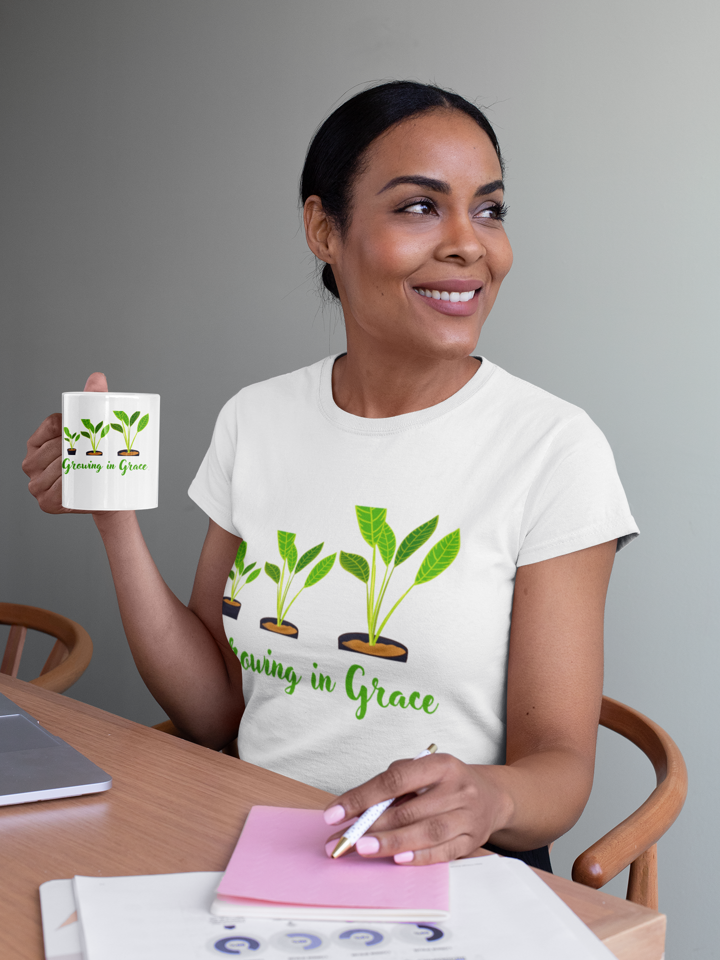 Woman holding a mug with a 'Growing in Grace' design, wearing a matching t-shirt, sitting at a table.
